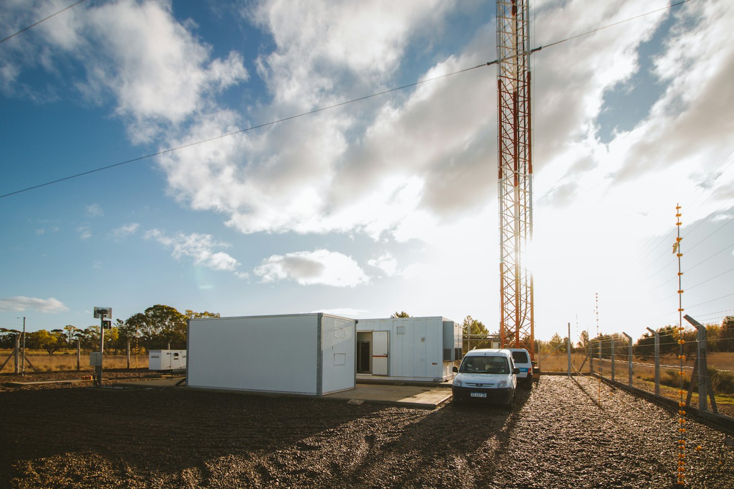 Two service vans parked at a telecommunications facility with a tower.